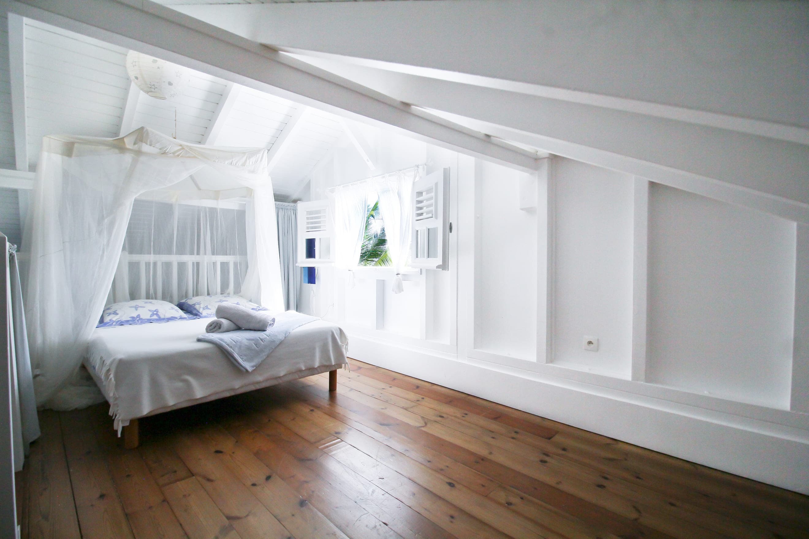 Troisième chambre de la Villa Alizé à l’étage, lit sous moustiquaire sur plancher bois