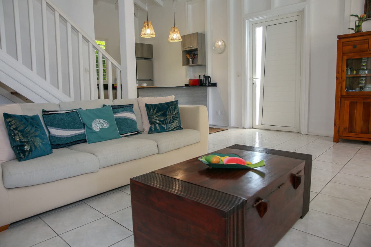 Canapé blanc, coussins turquoise et malle basse en bois dans le salon de la Villa Alizé