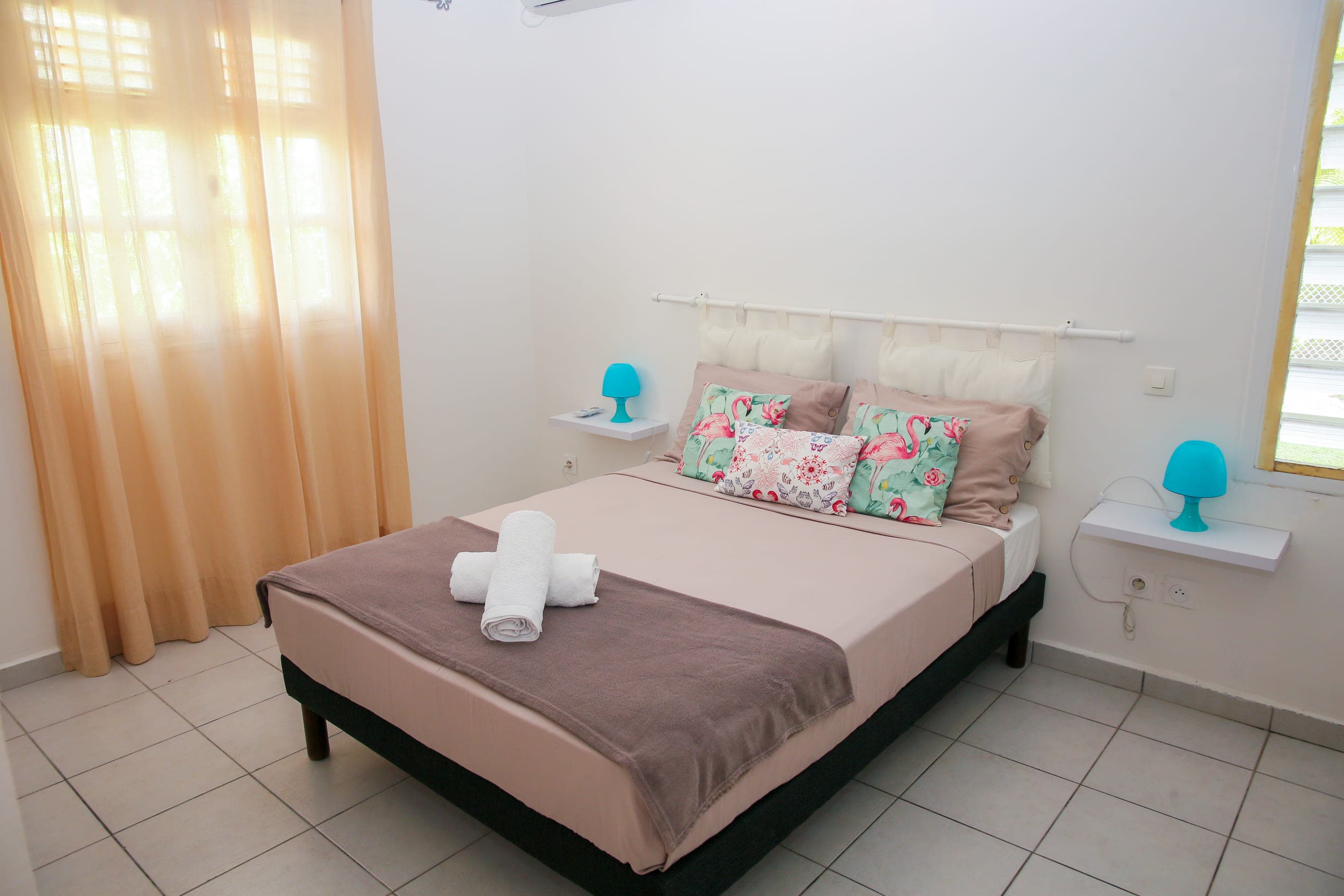 Deuxième chambre de la Villa Bahia, lit double, coussins fleuris et lampes turquoise