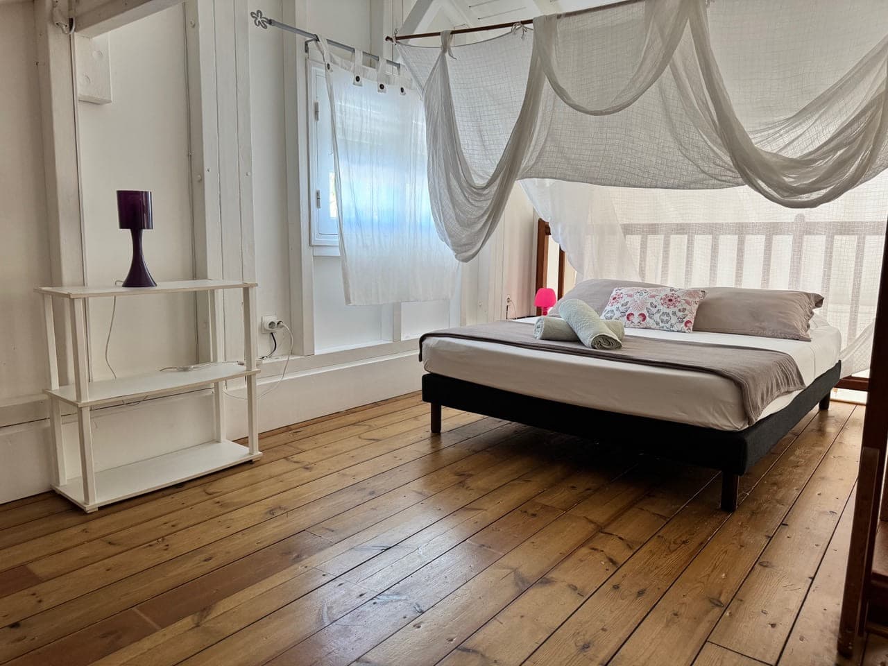La chambre à l'étage de la Villa Bahia, lit sous moustiquaire sur plancher de bois