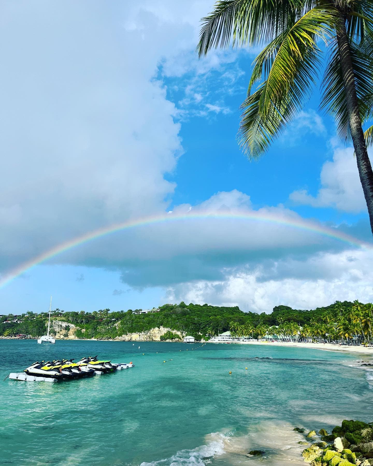 Jet skis amarrés dans une baie turquoise sous un arc-en-ciel