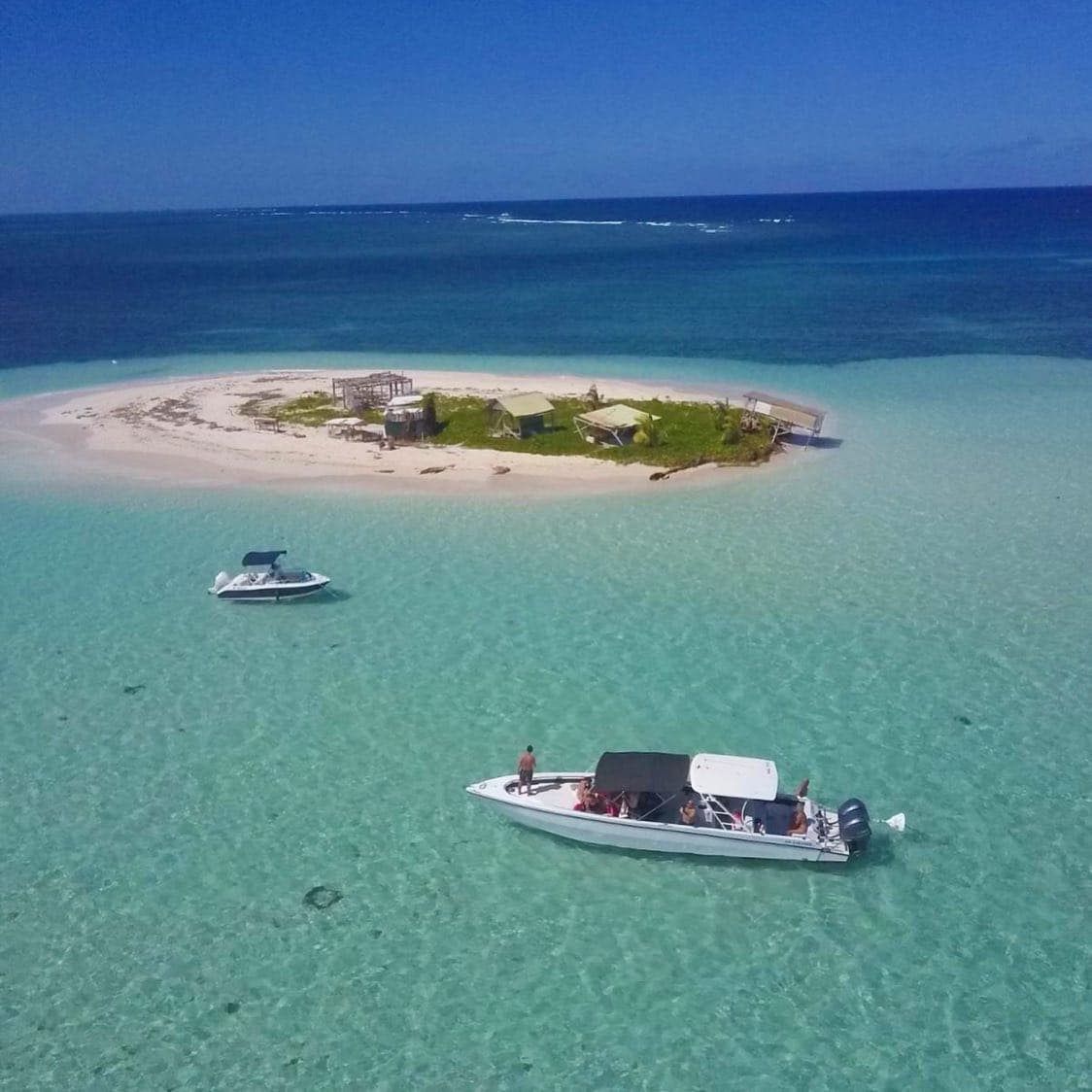 Îlet de sable blanc et bateaux au mouillage dans un lagon turquoise