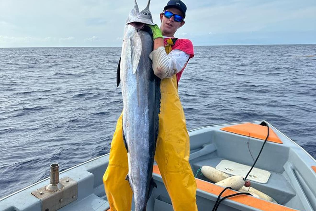 Un marlin tenu à bout de bras sur le pont, la mer ouverte derrière